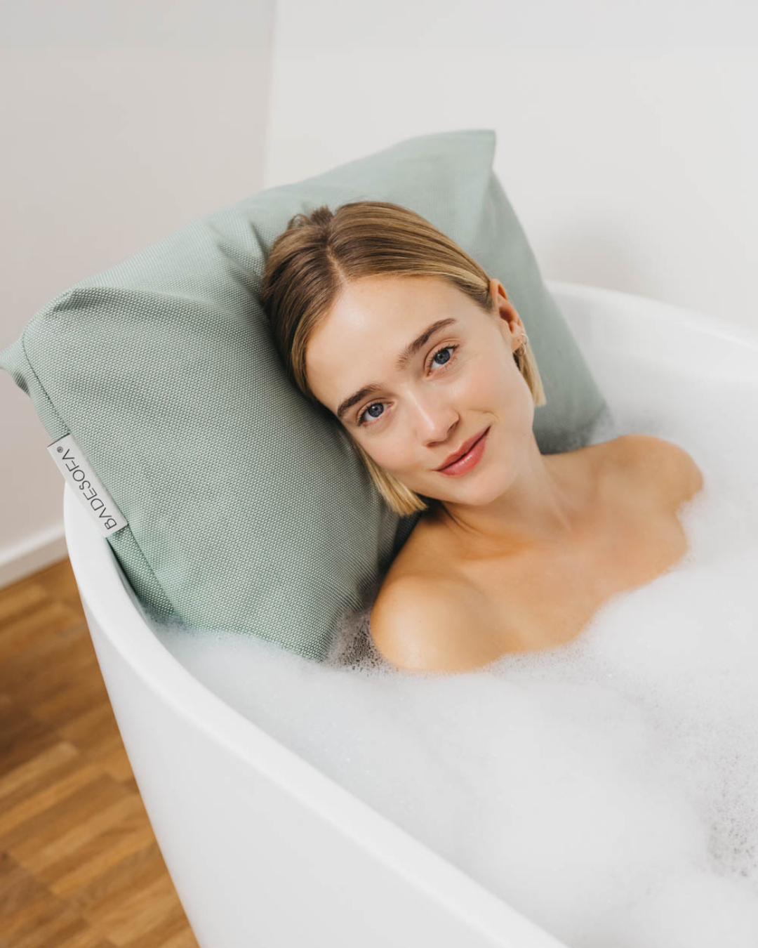 A photo of a woman relaxing in a bubble bath, resting against a BADESOFA Back Bath Pillow in color Green |