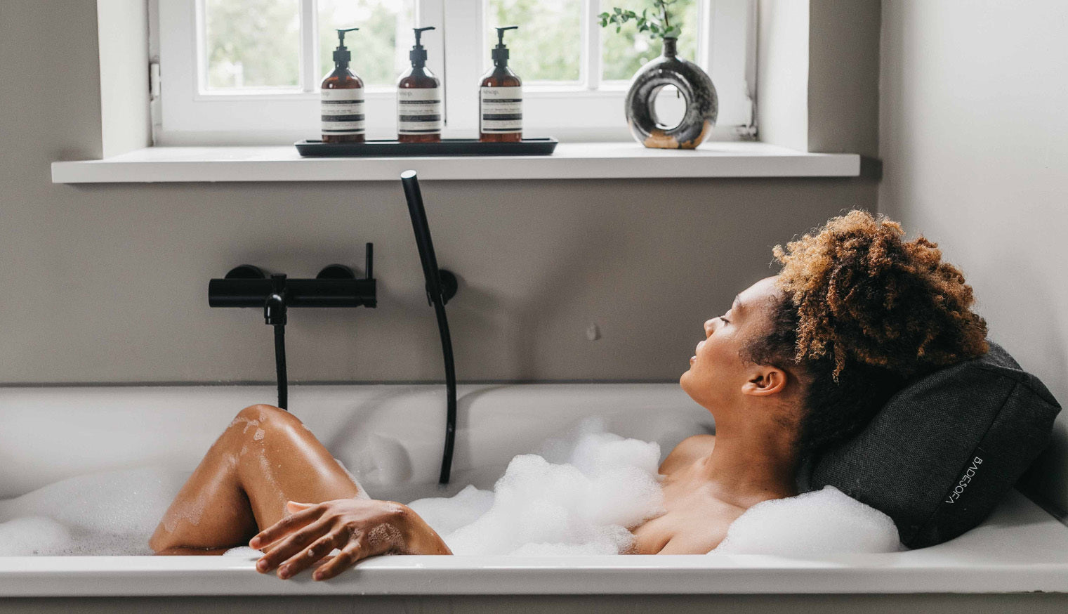 Frau liegt in der Badewanne, entspannt sich und genießt die Gerüche ihres Badeschaums